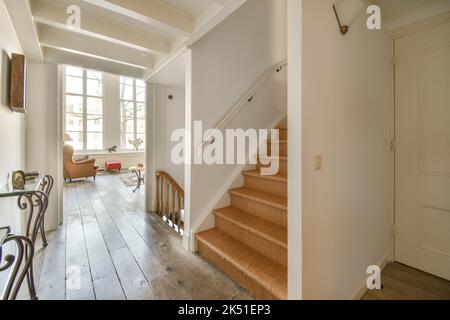 Intérieur de couloir spacieux avec escalier en bois décoré d'éléments ornementaux dans des rambardes et murs blancs menant à la salle de séjour Banque D'Images