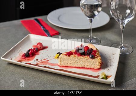 Morceau de délicieux cheesecake aux baies rouges et confiture servi sur une assiette rectangulaire près de verres d'eau dans le restaurant Banque D'Images