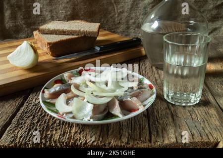 Vodka avec un en-cas sur la table. Nourriture sur fond sombre. Émincez le hareng avec les oignons dans une assiette Banque D'Images