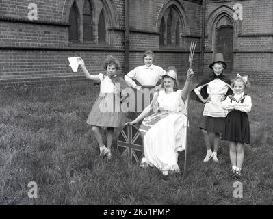 1961, historique, dans le domaine d'une église locale, un groupe de filles participant aux célébrations du printemps du jour de mai se posent ensemble pour une photo. Dans leurs costumes de parade, ils se tiennent autour d'une adolescente habillée comme la déesse Britannia, portant son casque Corinthian, robe et avec son trident et bouclier. Britannia, une femme guerrier, est une image qui remonte à la province romaine de Grande-Bretagne pendant l'Empire romain et a été ressuscité et est devenu une figure symbolique populaire dans les périodes ultérieures de l'histoire britannique, en particulier à l'âge de l'Empire. Banque D'Images