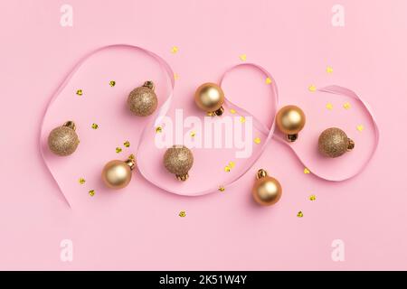 Carte de Noël avec boules dorées à paillettes, confettis en forme de coeur et ruban de satin sur fond rose Banque D'Images