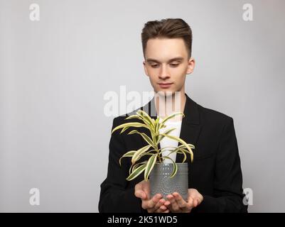 Portrait d'un jeune homme élégant portant un costume noir tenant une plante de maison en pot. Studio tourné sur fond gris Banque D'Images