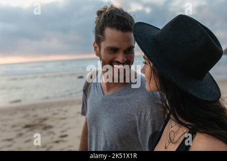 homme barbu gai regardant la femme en chapeau noir sur la plage, image de stock Banque D'Images