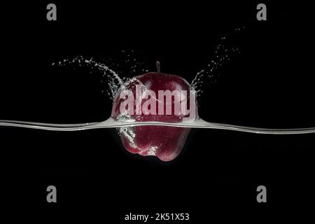 Projection de pomme rouge dans l'eau, vue d'un côté sur fond noir. Banque D'Images