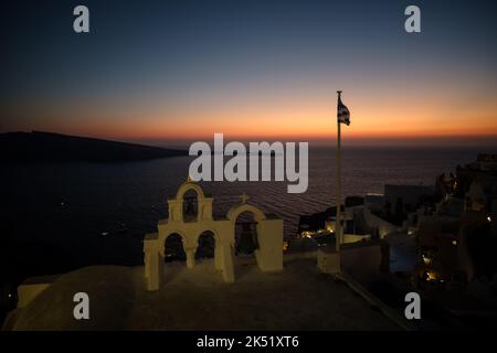 Vue sur le sommet d'une église avec des cloches, le drapeau grec et un coucher de soleil étonnant dans le fond de Santorini Grèce Banque D'Images