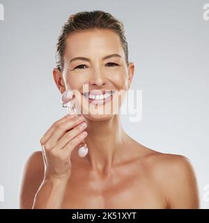 Rouleau de jade, soin du visage et femme mûre avec massage du visage de luxe sur fond gris maquette studio. Heureux, en bonne santé et sourire pour les personnes âgées Banque D'Images