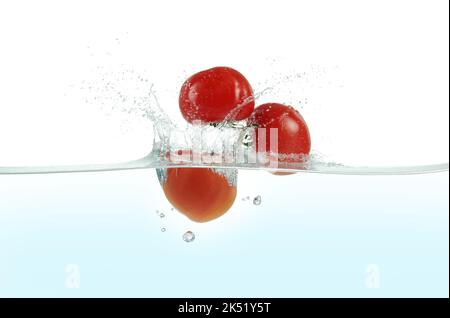 Trois tomates éclaboussant dans l'eau. Vue latérale sur fond blanc. Banque D'Images