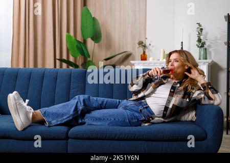 Femme du Prücasien située sur un canapé et buvant du vin rouge Banque D'Images
