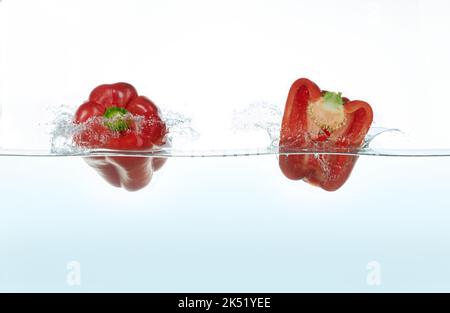 Deux poivrons rouges éclaboussant dans l'eau. Vue latérale sur fond blanc. Banque D'Images