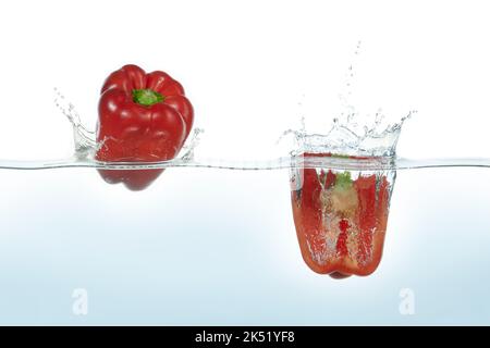 Deux poivrons rouges éclaboussant dans l'eau. Vue latérale sur fond blanc. Banque D'Images