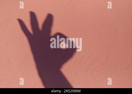 Ombre de la main qui a fait le signe ok sur fond de béton rose. Banque D'Images