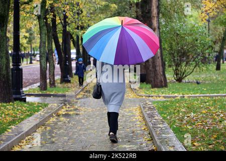 Pluie en ville, femme mince avec parapluie coloré portant un manteau gris marchant dans la rue. Temps pluvieux dans le parc d'automne Banque D'Images