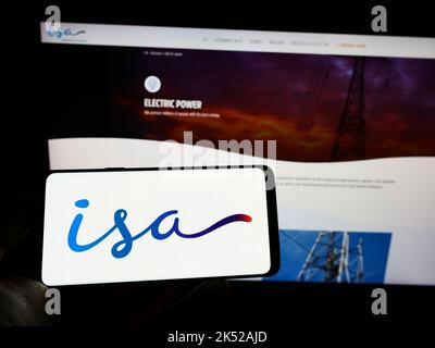 Personne tenant un téléphone portable avec le logo de la société colombienne Grupo ISA sur l'écran en face de la page web d'affaires. Mise au point sur l'affichage du téléphone. Banque D'Images