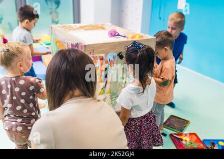 des groupes d'enfants d'âge préscolaire peignent sur le cellophane avec leur enseignant dans la pépinière. Photo de haute qualité Banque D'Images