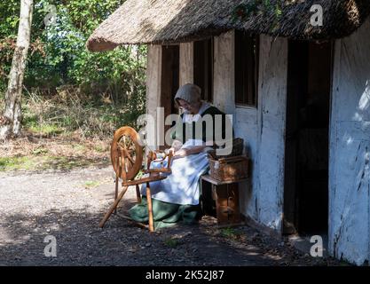 Femme en coton de costume traditionnel tournant sur une roue de spinning traditionnelle, petit village de loisirs médiéval Woodham, près de Gosport, Angleterre. Banque D'Images