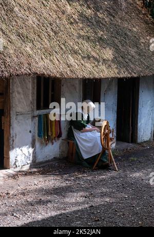 Femme en coton de costume traditionnel tournant sur une roue de spinning traditionnelle, petit village de loisirs médiéval Woodham, près de Gosport, Angleterre. Banque D'Images