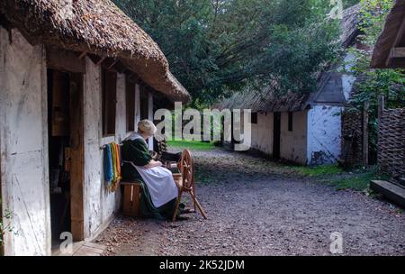 Femme en coton de costume traditionnel tournant sur une roue de spinning traditionnelle, petit village de loisirs médiéval Woodham, près de Gosport, Angleterre. Banque D'Images