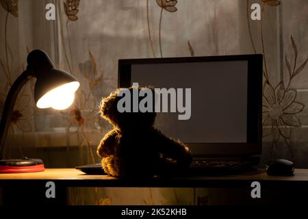 ours en peluche pour enfants assis portant un ordinateur portable sur la table, portant une lampe de table dans les chambres la nuit, portant des fenêtres, solitude, joie dans une la Banque D'Images