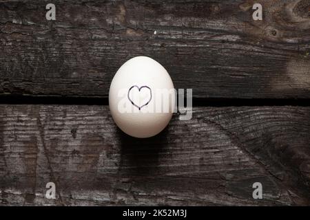 le coeur est tiré sur un œuf de poulet qui se trouve sur une vieille table en bois, l'amour et les sentiments Banque D'Images