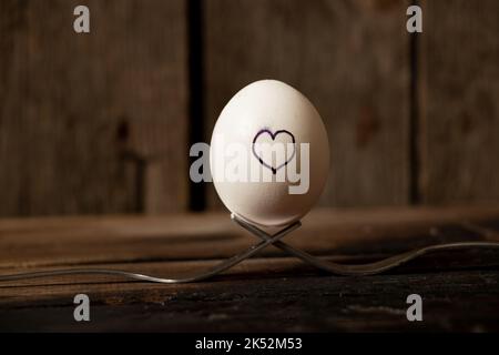 le coeur est tiré sur un œuf de poulet qui se trouve sur des fourchettes sur une vieille table en bois, l'amour et les sentiments Banque D'Images