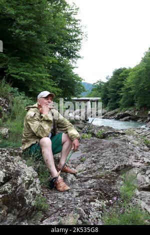 Homme senior assis sur la rive de la rivière Belaya dans la gorge de granit, Adygea Banque D'Images
