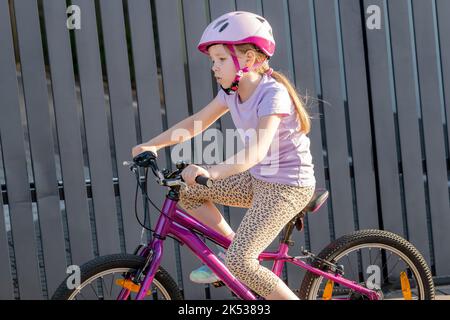 Fille d'âge scolaire à vélo, portant un casque, jeune cycliste enfant dans la rue, à proximité, vue latérale, une personne. Vélo pour enfants, de près, enfants et Banque D'Images