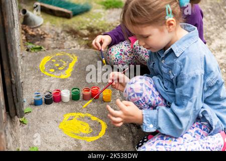 Les jeunes enfants peignent sur le béton, deux filles, l'art, l'activité en plein air. Les petits enfants répandent de la peinture colorée sur le sol à l'aide de pinceaux, scène extérieure Banque D'Images