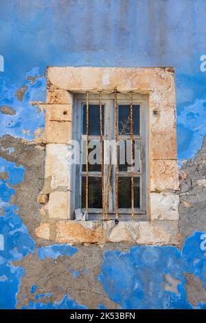 peinture caillée en chagis, peinture à l'état de surface texturée sur un ancien bâtiment grec, fenêtre grecque avec une peinture bleue qui s'écaille au soleil, fenêtre barrée. Banque D'Images