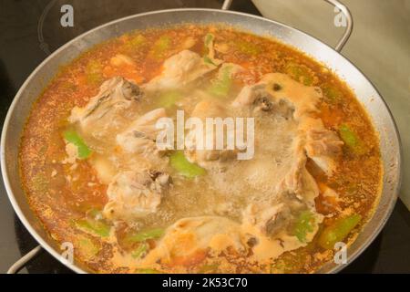 Image d'une paella Valencienne en cours de préparation avec de l'eau bouillante dans une table de cuisson en céramique maison Banque D'Images