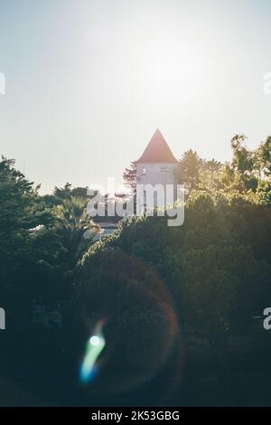 Un contraste vertical avec une tour d'un bâtiment ancien ou un château avec un toit triangulaire conique rétroéclairé par lumière du soleil de soirée éclat de lentille Banque D'Images