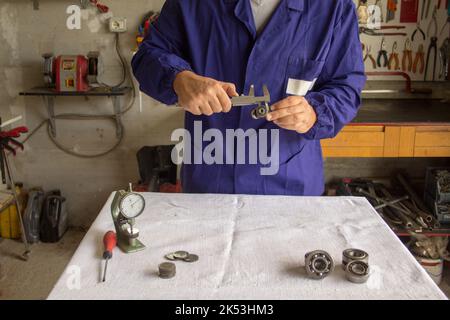 Mains d'un mécanicien qui, dans son atelier, mesure une voiture de travers avec un calibre. Mécanique de précision. Banque D'Images