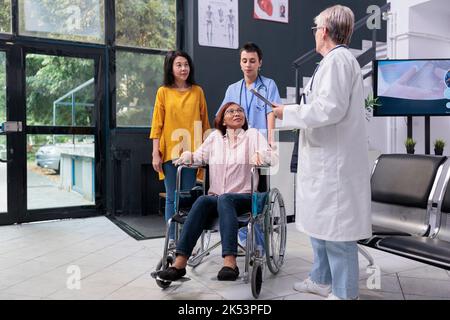 Le personnel médical discutant avec le patient blessé avant de consulter un médecin dans la salle d'attente de l'hôpital. Médecin médecin médecin donnant des conseils médicaux à une femme asiatique pendant un examen de réadaptation. Support médical Banque D'Images