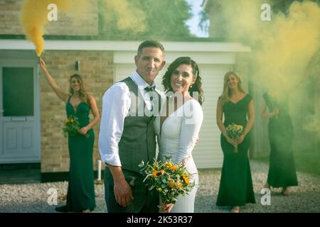 Couple marié regardant l'objectif, deux demoiselles d'honneur tenant des fusées éclairantes et la troisième regarde, j'ai fait un couple regardant dans l'appareil photo demoiselle d'honneur avec des fleurs regardant sur Banque D'Images