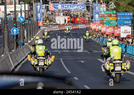 Un groupe de gardes civils espagnols sur des motos traversant une route pavée avec des panneaux et des personnes en arrière-plan. Banque D'Images