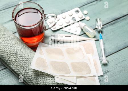 Emplâtres à la moutarde avec médicaments, thermomètre, tasse de thé et serviette sur fond de bois de couleur Banque D'Images