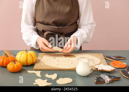 Femme faisant des biscuits d'Halloween à la table près du mur rose Banque D'Images