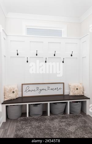 Un mudroom confortable avec des crochets sur le bord et des murs de lattes, une banquette en bois et un tapis sur un sol carrelé. Banque D'Images