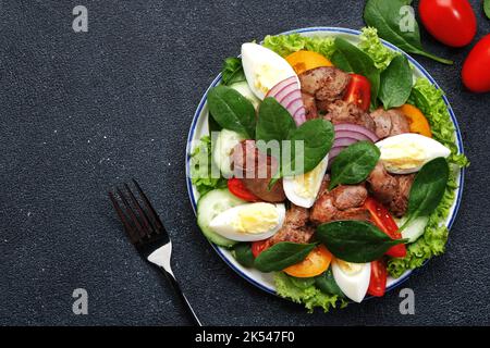 Salade Périgord avec foie de poulet, tomates, concombres, œufs, laitue et épinards. Arrière-plan de la table de cuisine noire, vue du dessus Banque D'Images