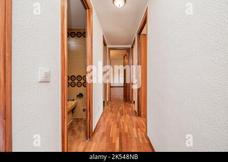 Couloir d'une maison urbaine vide avec parquet rougeâtre avec accès à plusieurs chambres et murs peints en gotelette blanche Banque D'Images