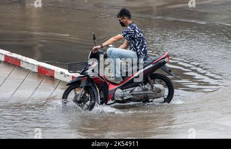 SAMUT PRAKAN, THAÏLANDE, OCT 04 2022, Un homme sur une moto conduit à travers une grande flaque avec ses pieds vers le haut Banque D'Images