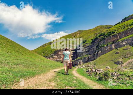 Une fille avec une valise marche le long d'une route de terre dans les montagnes. Voyage intéressant de la femme solitaire Banque D'Images