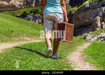 Une fille avec une valise marche le long d'une route de terre dans les montagnes. Voyage intéressant de la femme solitaire Banque D'Images