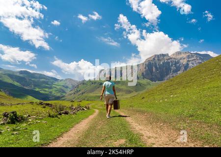 Une fille avec une valise marche le long d'une route de terre dans les montagnes. Voyage intéressant de la femme solitaire Banque D'Images