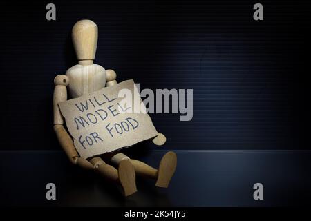 Un mannequin en bois assis tenant un panneau « will Model for Food » dans un éclairage d'ambiance sombre et doux, capturé dans un studio Banque D'Images