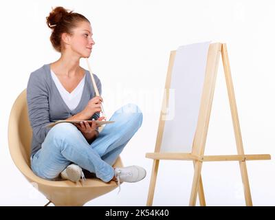 Attente de l'inspiration à frapper. Photo studio d'une jeune femme artiste assise sur une chaise et regardant une toile vierge. Banque D'Images