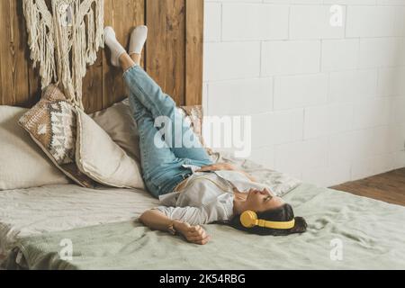 Une belle femme aux cheveux foncés est couché sur le lit à la maison dans un casque. Banque D'Images