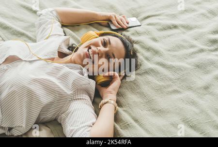 Une belle femme aux cheveux foncés est couché sur le lit à la maison dans un casque. Banque D'Images