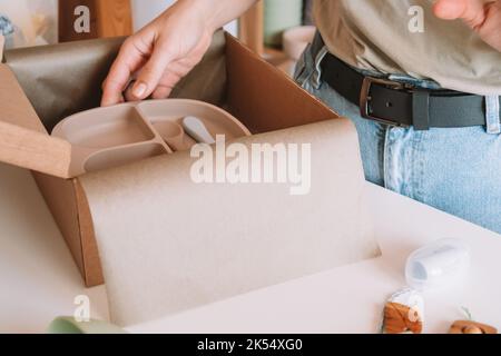 Image rognée des mains de femme emballage et emballage de l'expédition avec des plats en silicone pour enfants dans une boîte en carton pour la livraison. Jouet en bois de hochet, trinket Banque D'Images