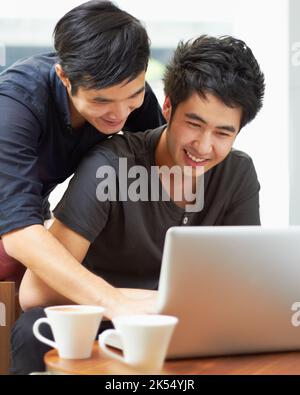 Celui-ci a l'air parfait. Un jeune couple gay utilisant un ordinateur portable à l'intérieur. Banque D'Images