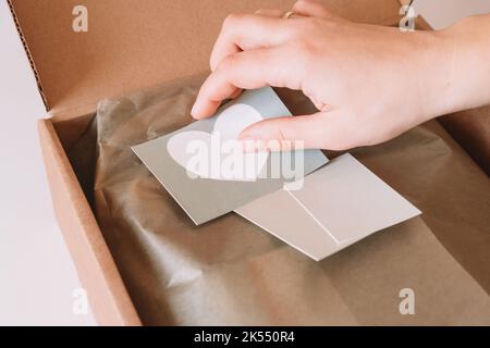 Photo rognée des mains de femme d'affaires emballage, préparation du colis pour livraison à l'acheteur, mise des cartes postales dans la boîte. Propriétaire de petite entreprise Banque D'Images